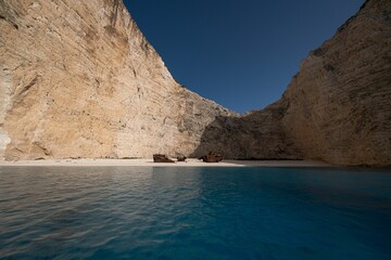 Calm ocean and rusted shipwreck on the sandy shore with cliffs on a sunny day in Zakynthos, Greece