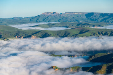 Low clouds cover the low green mountains in the mountainous area of the Elbrus region