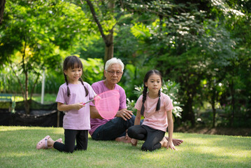 Fototapeta premium Happy Asian family children having fun and catches a net of insects with her grandfather in the park