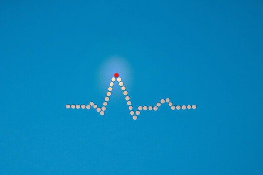 Medical ECG heart wave made from white tablets against a blue background. A red tablet marks the highest point. Clinical concept. Editorial medical heart related picture. EKG cardiac trace.
