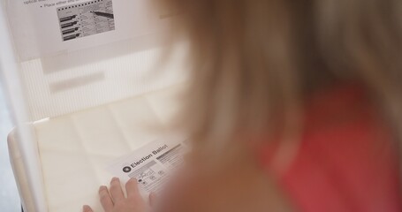 Close, over the shoulder view of young woman voter filling in a ballot at a voting booth in the...