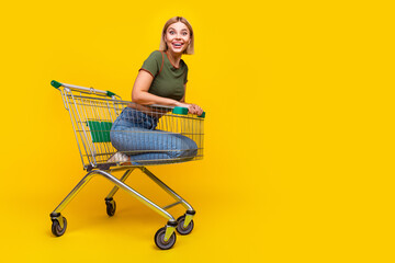 Full size photo of impressed girl dressed khaki crop top sit in shopping cart near logo empty space...