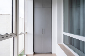 Fototapeta premium Modern grey wardrobe on a glazed bright balcony with large windows