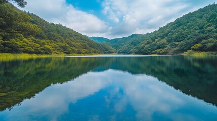 Fototapeta premium A tranquil stock photo of a calm lake surrounded by dense forest and rolling hills.