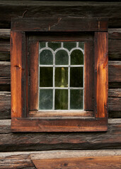 Old Natural Wood Window with Colored Glass on a log house at a Norwegian Open-Air Museum: Photographed from Outside with a Wine Bottle Visible Inside, Showcasing Traditional Design and Craftsmanship