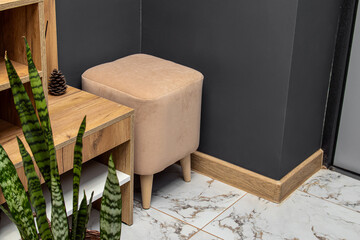 Beige square pouf with wooden legs in hallway. Velour upholstery