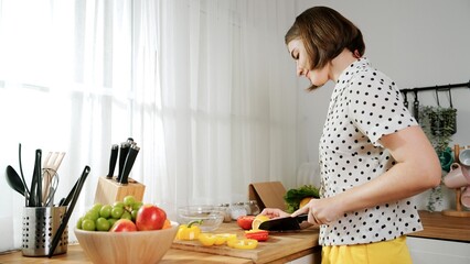 Energetic mother making salad for breakfast at modern kitchen while chopping vegetable surrounded with kitchenware. Smart female house keeper cooking and preparing food. Healthy lifestyle. Pedagogy.