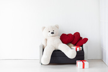 Interior of a white room with a gray sofa and a red gift toy bear
