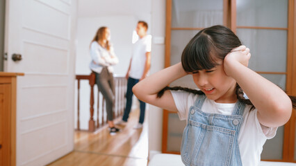 Obraz premium Stressed and unhappy young girl huddle in corner, cover her ears blocking sound of her parent arguing in background. Domestic violence at home and traumatic childhood develop to depression. Synchronos