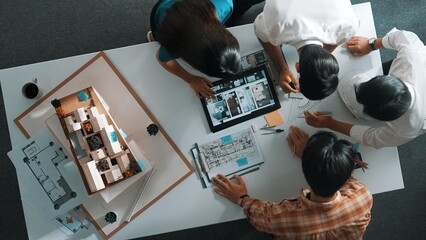 Top down view of architect engineer team discussing and point at tablet display construction at table with blueprint and house model at meeting. Diverse designer planning design house. Alimentation.