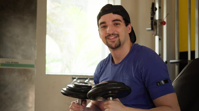 Man Finishing Workout, Smiling at the Camera. Confident Man Enjoying His Gym Routine, Smiling After Completing a Dumbbell Exercise. Video concept of healthy life, good habits and gym advertising.