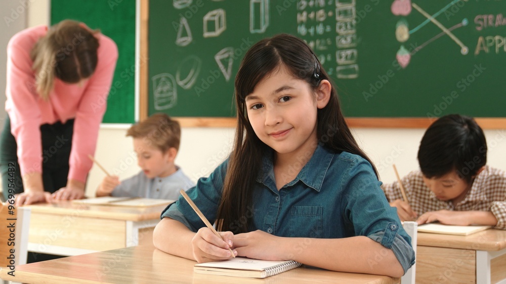 Aufkleber asian girl writing test or classwork while looking at camera at classroom. diverse happy student tak