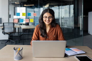 Young beautiful woman working inside office with laptop, business woman typing on keyboard, happy...