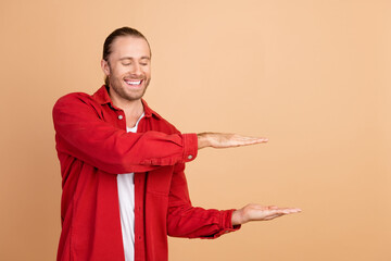 Photo of nice young man arms show empty space wear red shirt isolated on beige color background