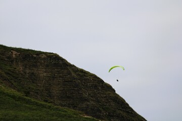 a paraglider in the sky and a rocky cliff with green plants in the foreground