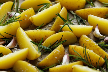  Rawpotato wedges seasoned with rosemary and garlic prepared for baking, top view