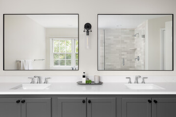 A bathroom with a grey vanity cabinet, white marble countertop with two sinks, and a view through the large mirrors of the tiled shower and window.