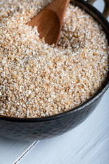 Cracked wheat in bowl on white table. Crushed wheat with wooden spoon. Close-up.