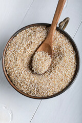 Cracked wheat in bowl on white table. Crushed wheat with wooden spoon. Close-up.