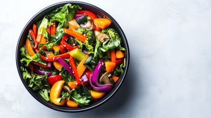 Colorful healthy vegetable salad in a black bowl, featuring bell peppers, broccoli, onions, and leafy greens on a light background.