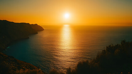 A majestic ocean view from a mountaintop with the sun setting over the sea and casting a golden glow on the water.