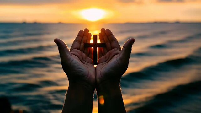 Hands holding a cross in front of a beautiful sunset over the ocean at a serene beach location