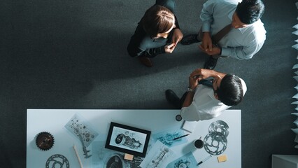 Top down view of smart engineer talking about turbine engine design while standing at meeting table with gear. Aerial view of technician discussing about electronic generator structure. Alimentation. © InfiniteFlow