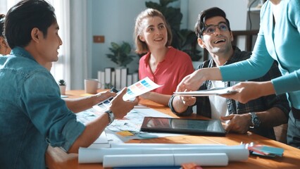Professional civil engineer handed document while looking at blueprints. Skilled architect team brainstorming idea and planning building design while sitting at meeting table with plans. Symposium.