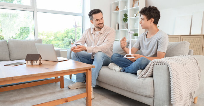 Teenage boy and his father with wind turbine models sitting on sofa at home