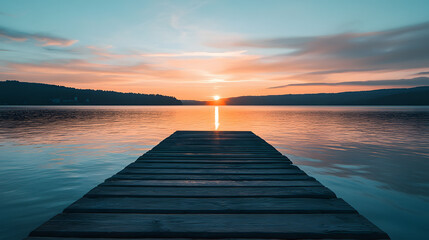 Obraz premium A tranquil ocean view from a peaceful pier with the sun setting behind distant hills and calm water reflecting the sky.