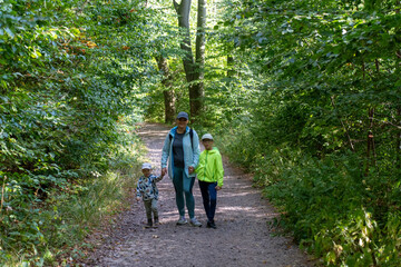 Obraz premium Mother with two children walking on a forest path during a sunny day, enjoying nature and spending time together outdoors. Concept of family bonding, outdoor activities, and healthy lifestyle. High