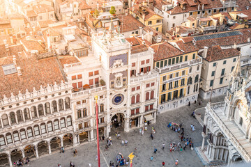 The majestic St Marks Clocktower stands prominently at sunset, surrounded by bustling crowds in the historic Piazza San Marco in Venice, Italy. Architectural beauty and lively atmosphere combine.