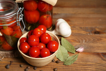 Jars and bowl with canned tomatoes on wooden background