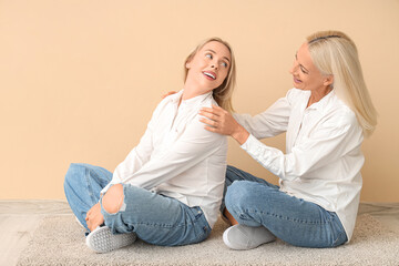 Happy young beautiful woman with her mother sitting on floor near orange wall