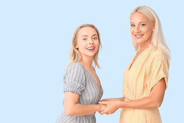 Happy young beautiful woman with her mother holding hands together on blue background