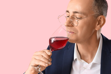 Mature man tasting red wine on pink background, closeup