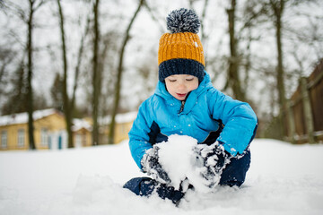 Adorable toddler boy having fun in a city on snowy winter day. Cute child wearing warm clothes playing in a snow.