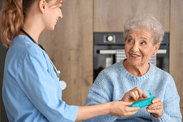 Senior woman with doctor taking pills in kitchen