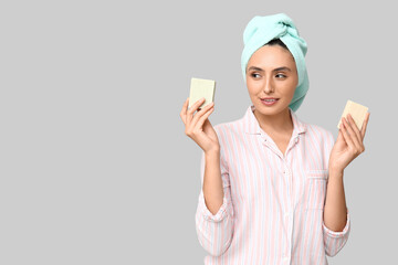 Young woman with soap bars on light background
