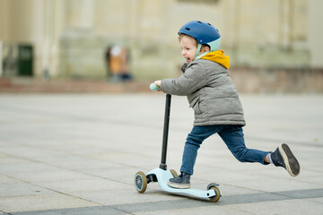 Adorable little boy riding his scooter in a city on autumn day. Young child riding a roller. Active...