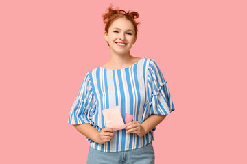 Beautiful young woman with menstrual cup and pad on pink background