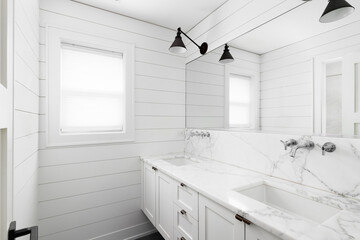 A farmhouse style bathroom detail with shiplap walls, a white floating vanity cabinet, and lights...