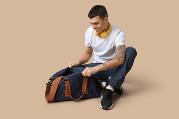 Young man with sports bag on beige background