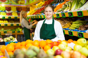 Obraz premium Portrait of smiling young girl wearing apron standing in fruit and vegetable store. First job concept..