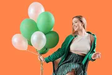Young woman with balloons sitting in chair on orange background