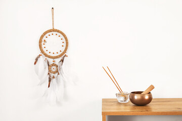 Tibetan bowl with aroma sticks and dream catcher on light wall in room