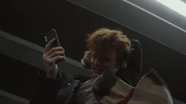 Low angle shot of angry young man hysterically making phone call, putting scarf around neck, clenching teeth and fist, touching hair under bridge