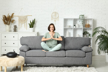 Young woman meditating while sitting on sofa at home