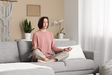 Young woman meditating while sitting on sofa at home