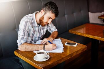 Man, coffee shop and writing with paperwork for small business as manager for inventory or stock. Male person, table and planning for food menu, restaurant or bistro as owner in hospitality industry